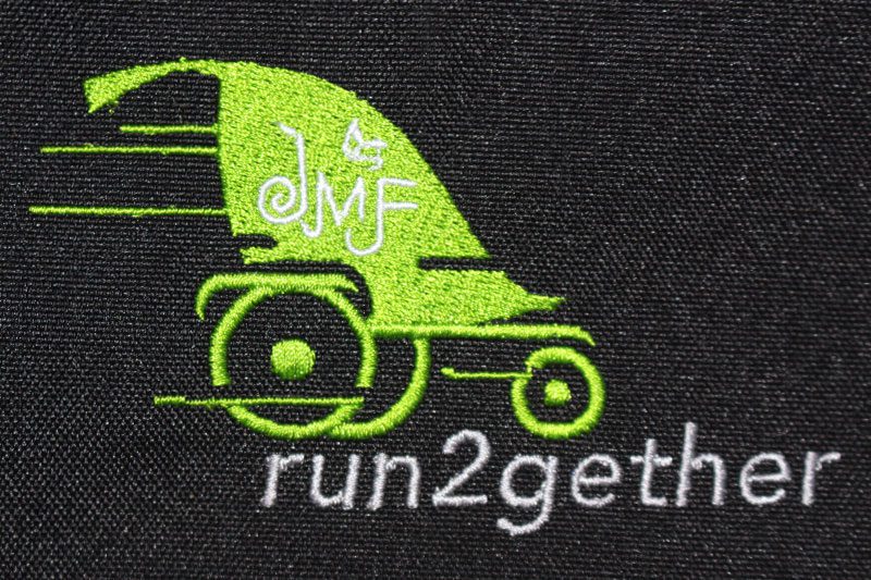 Green wheel-chair for running with JMF logo and text below that reads run2gether