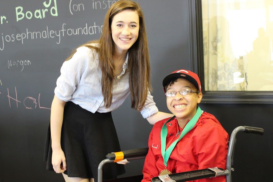Young Adult female smiling for a picture with a happy African-american girl in a wheelchair with award metal around her neck