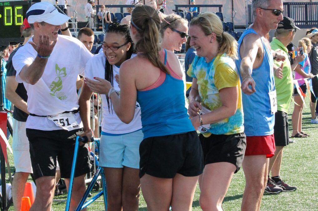 male and female runners standing and cheering around African American girl with walker