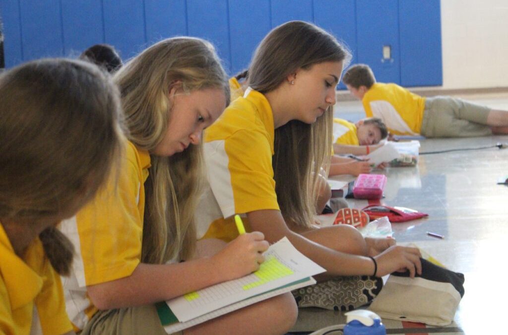 middle-school-aged children in yellow and white uniforms sitting on a gym floor