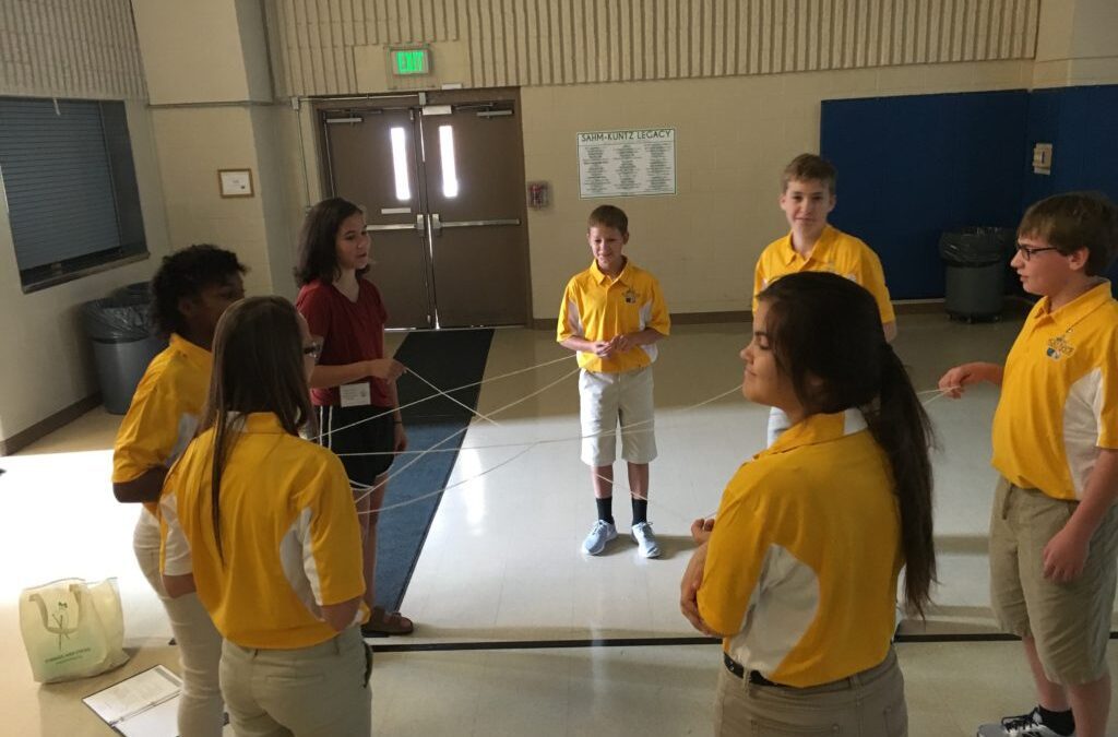 7 Middle school aged students in uniform standing in a circle doing an exercise with yarn to discuss the Butterly effect