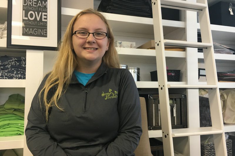 Junior board member Ashley Parker smiling in front of white bookcase at JMF offices