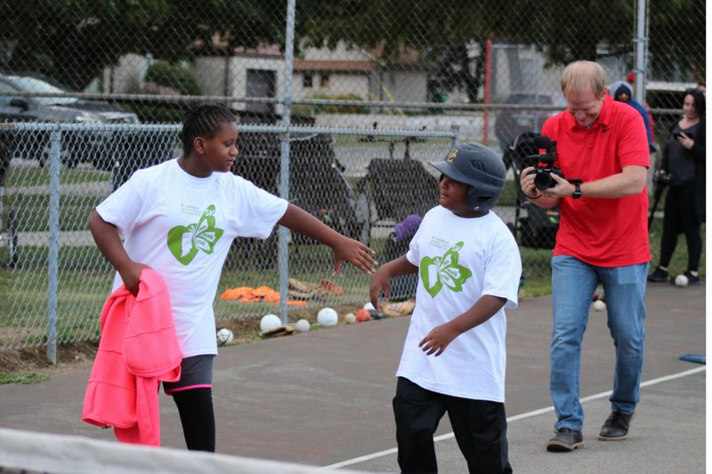 photo of two kids, one reaching for the other's hand who has a helmet on to go play softball