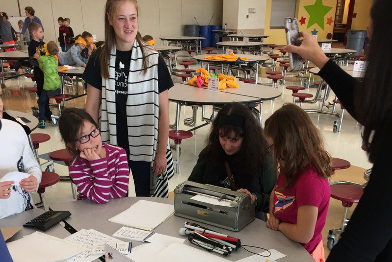 Teenage volunteer standing by table helping younger students during disability awareness training.