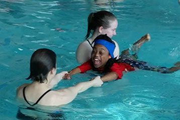 Young participant with coaches during adaptive swim class.