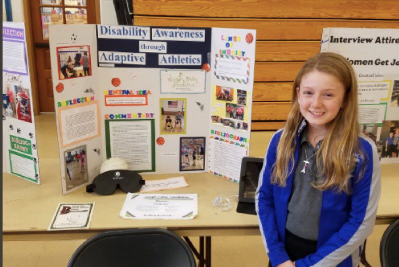 Female elementary student standing in front of a display sign.
