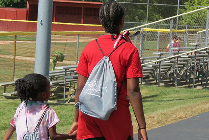 Image from behind of older sibling walking with their younger sibling to the Joseph Maley Foundation Sibs Summer Camp.