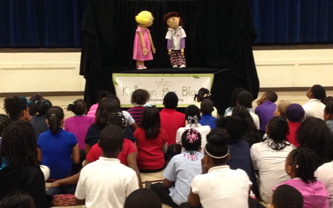 Group of students sitting on the ground watching a Joseph Maley Foundation puppet show.