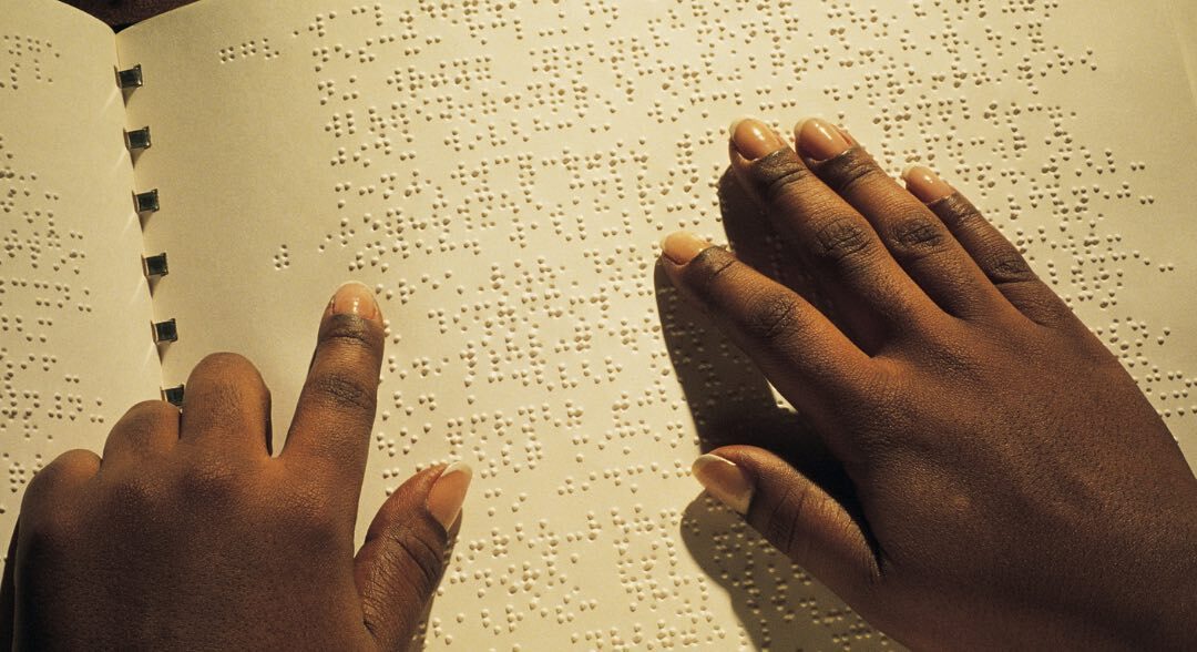 Two black hands reading braille from a book.