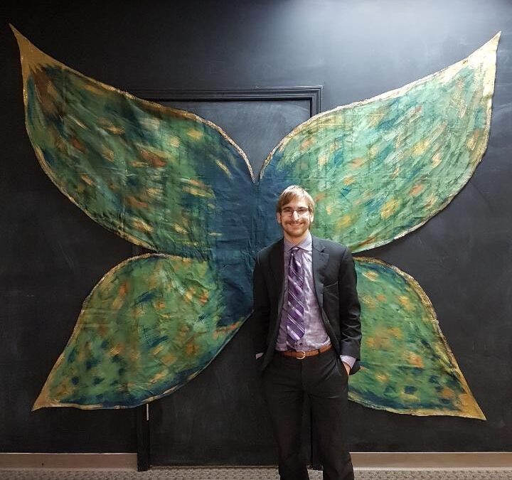 Ayden Kent standing and smiling in front of green butterfly wings