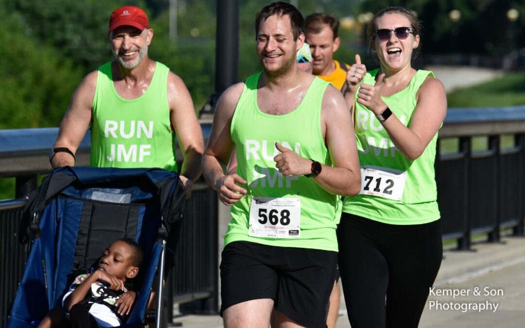 Group of four runners wearing green JMF tank tops and one of them pushing a stroller with an African American boy in it