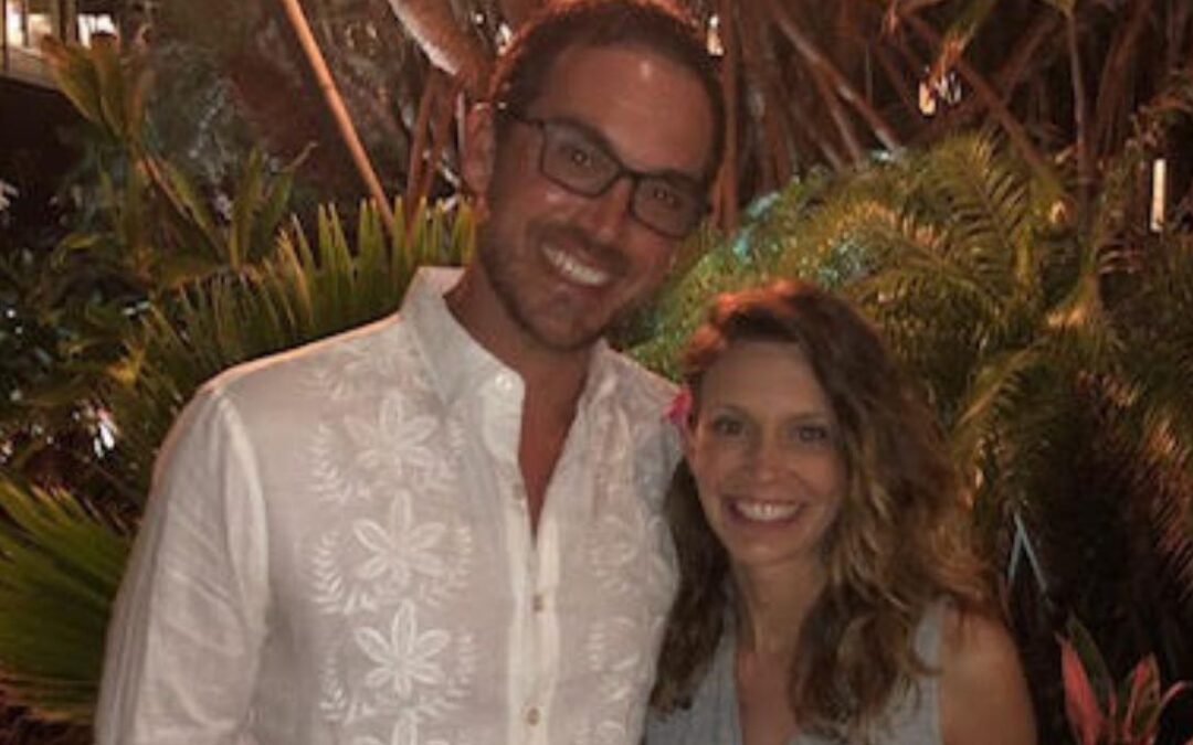 Melissa Gee with male partner posing for a picture in front of tropical trees